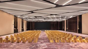 Ein Konferenzraum mit Reihen von Stühlen, einer Bühne und einem modernen Deckenstil.
