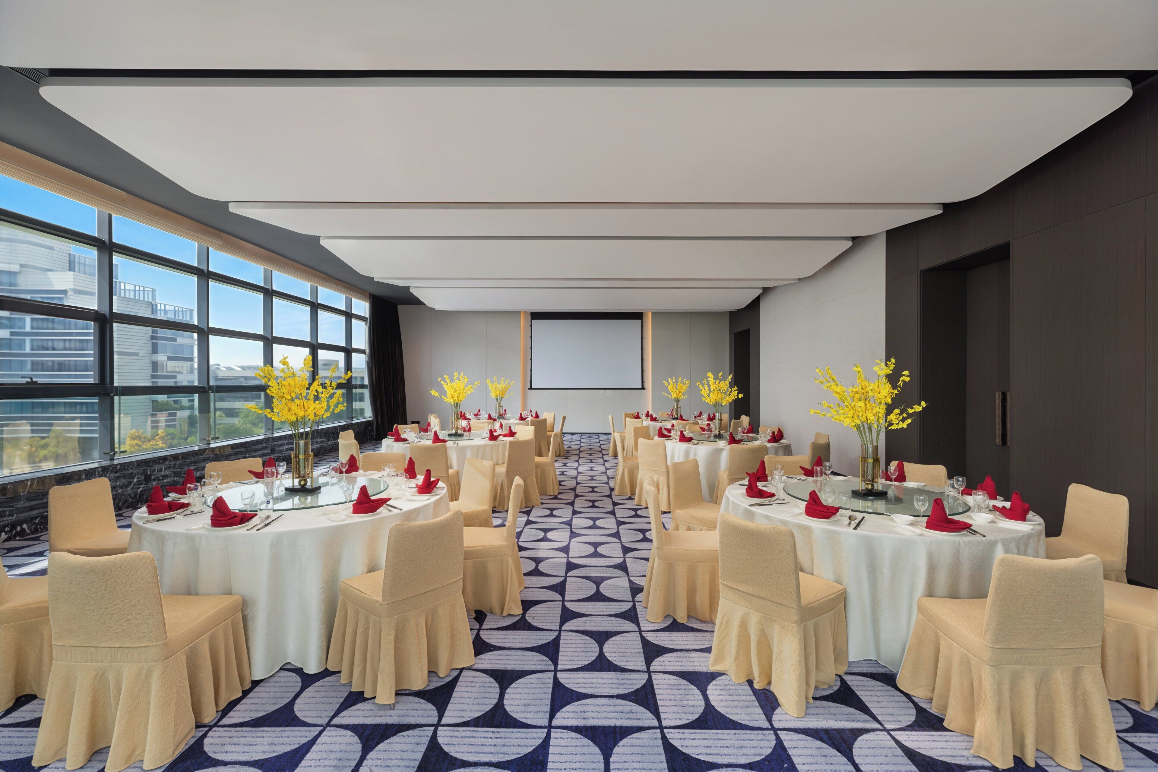 A conference room with round tables, chairs, and yellow flower arrangements.