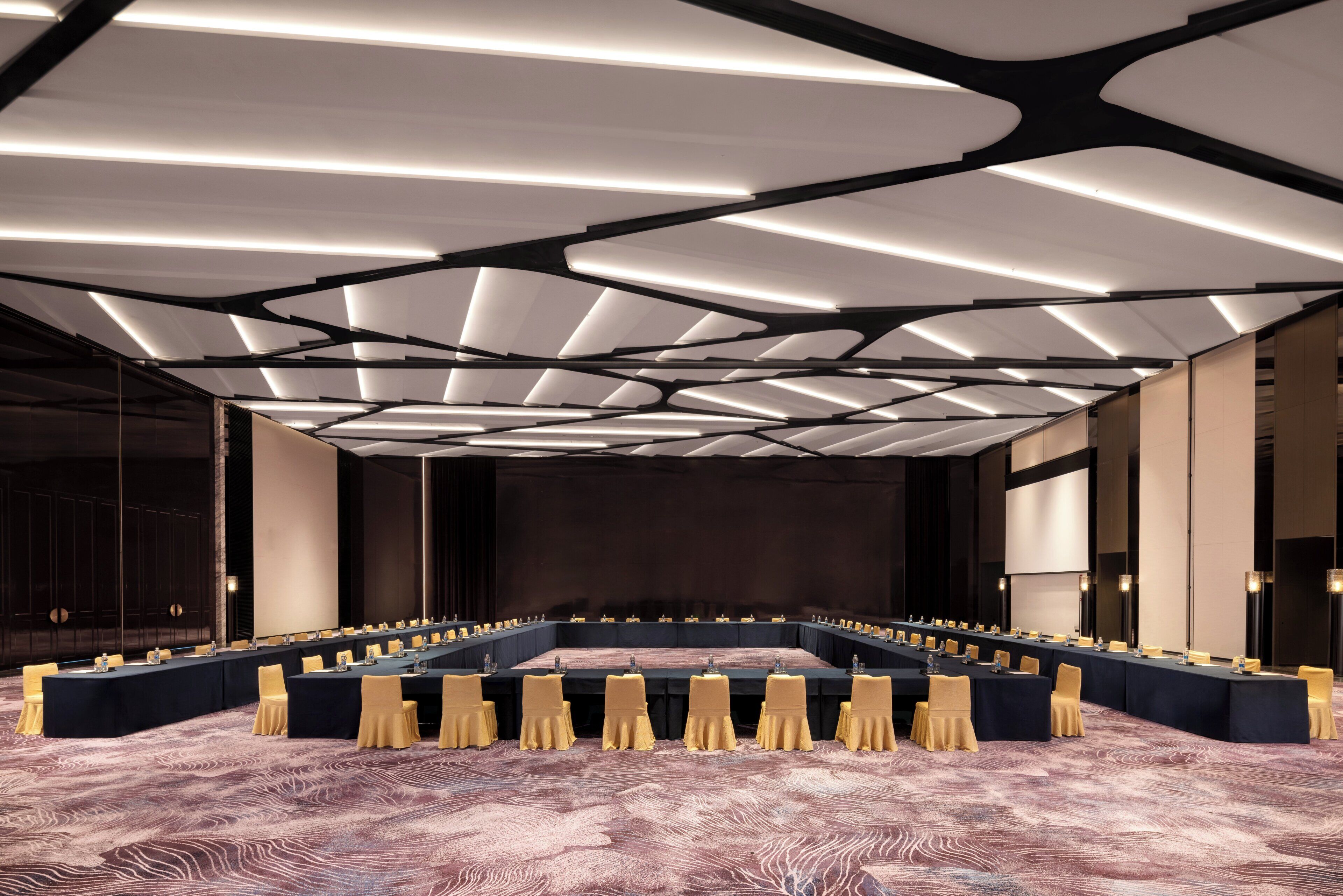 Un salón de conferencias con una mesa larga, sillas y una alfombra estampada.