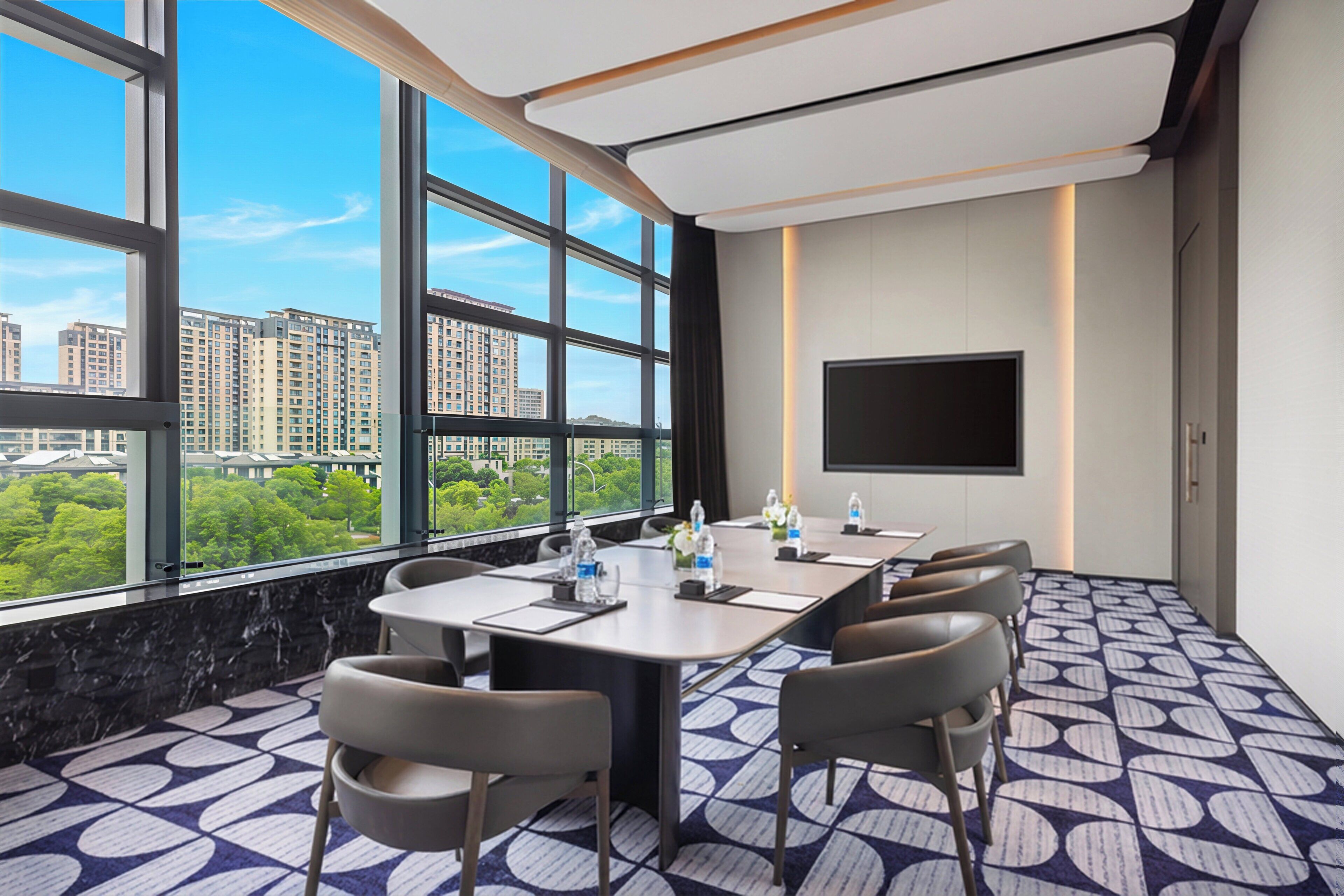 A conference room with a large window, a flat-screen TV, and a city view.