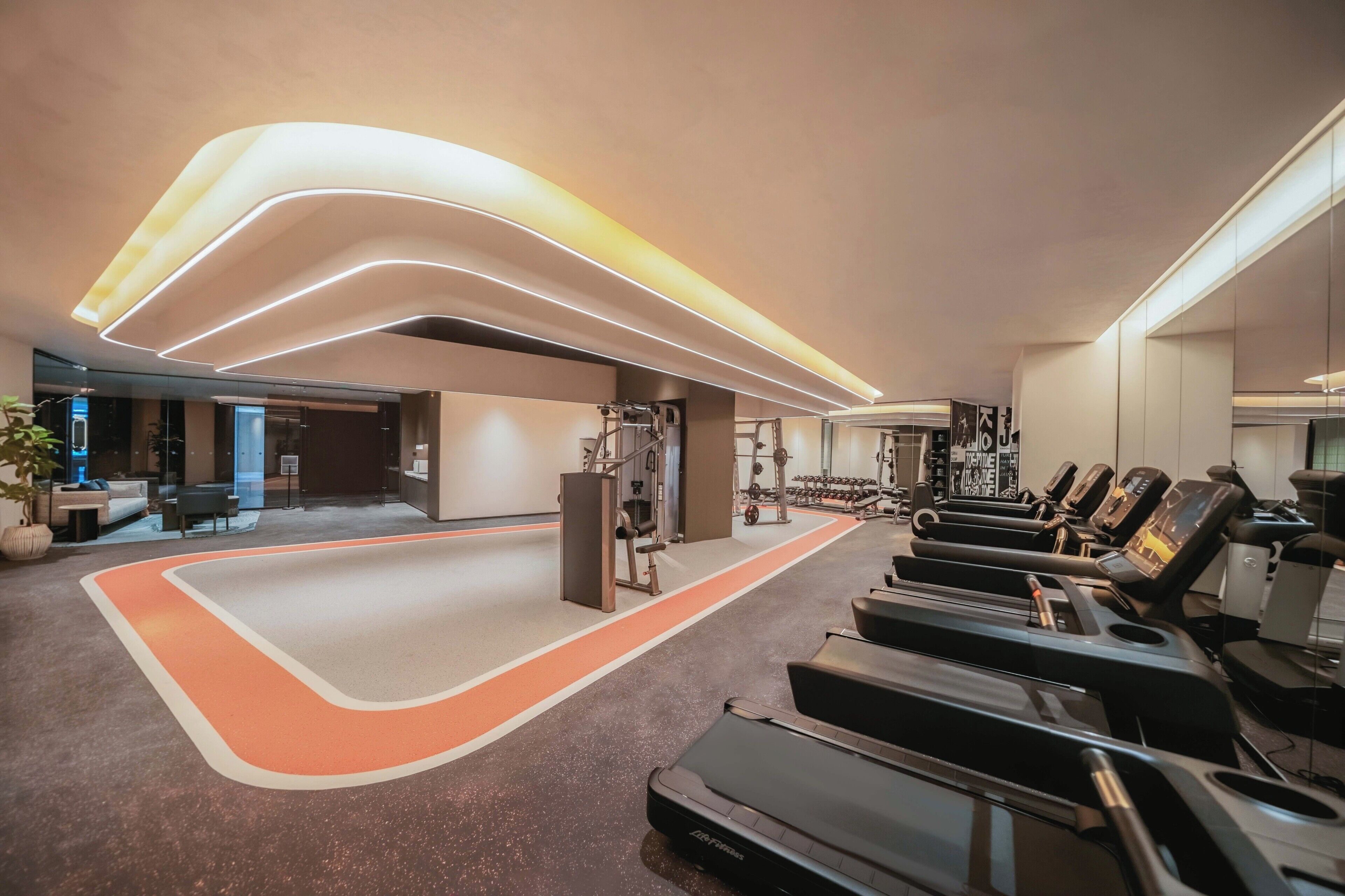 Ein modernes Fitnessstudio mit Laufbändern, Kraftgeräten und einem Bereich für Yoga-Matten.
