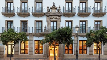 Un edificio con varios balcones, una entrada central y árboles en la parte delantera.