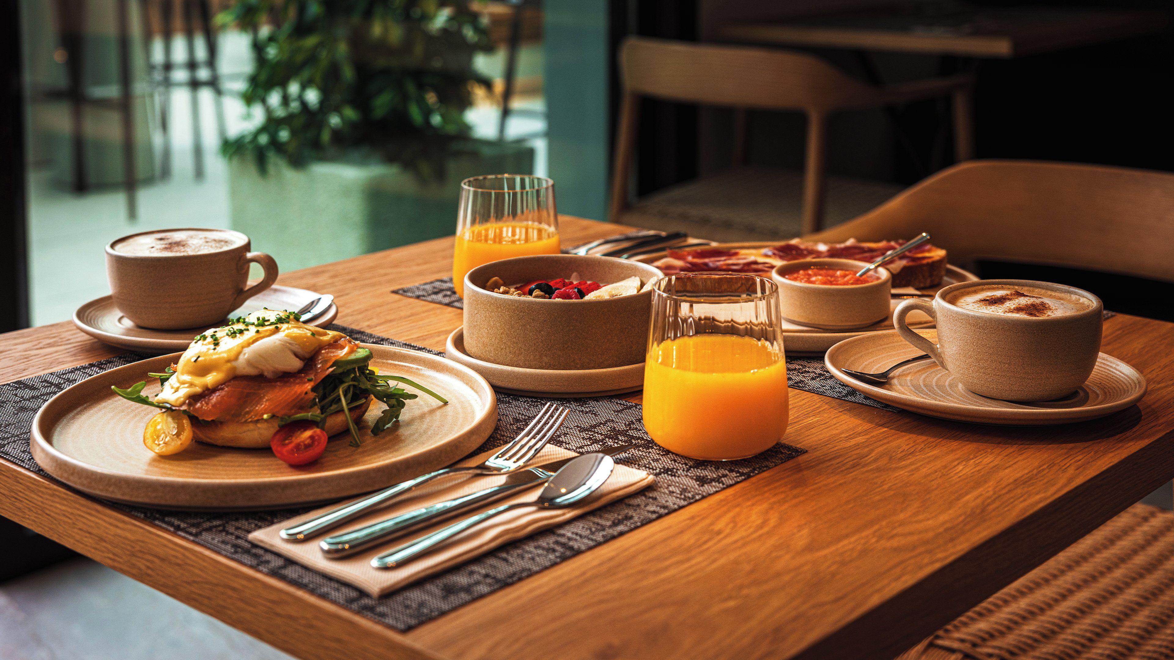 Une table en bois dressée pour le petit-déjeuner, avec une assiette de nourriture, un verre de jus d’orange et une tasse de café.