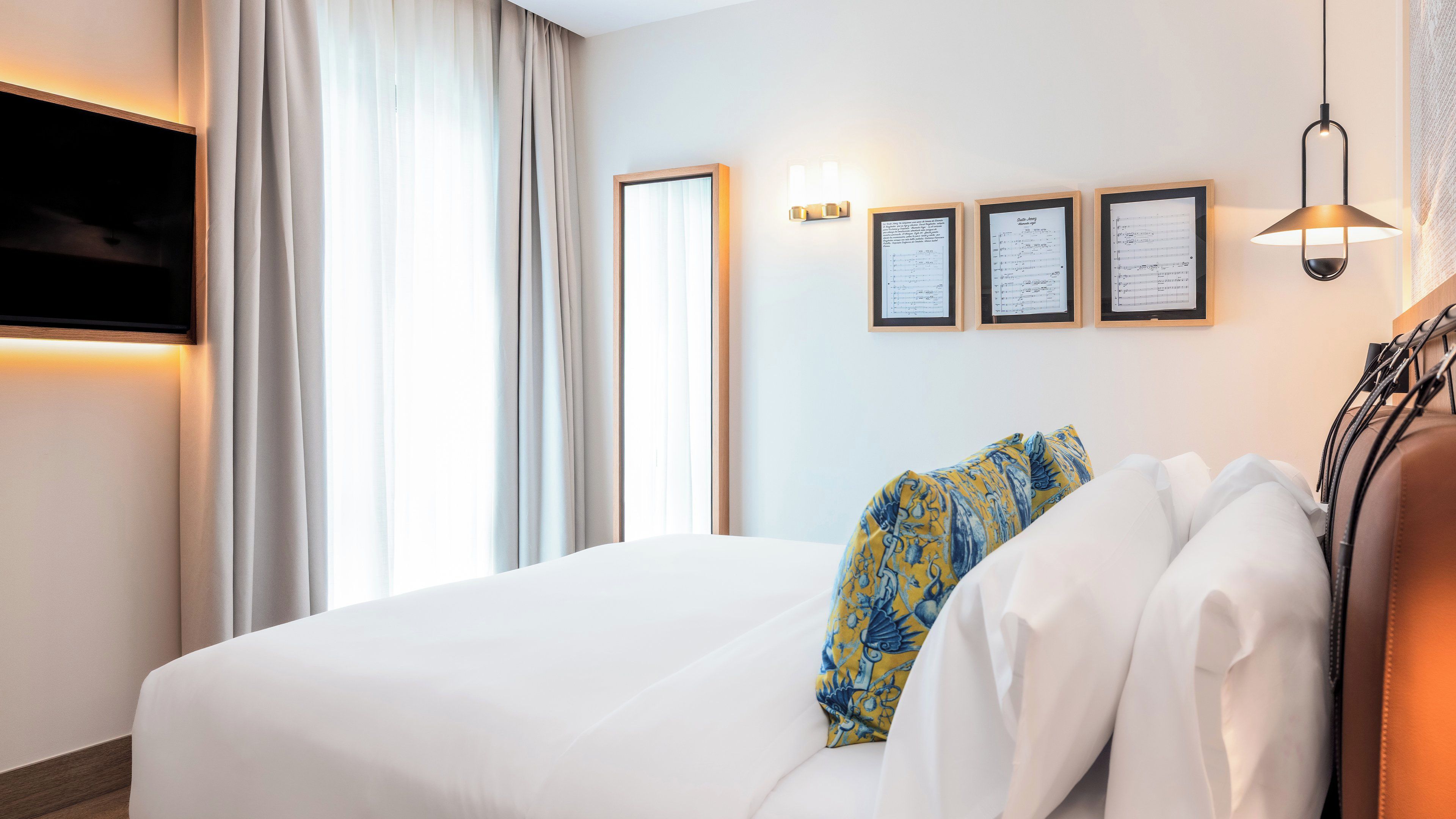 Habitación de hotel con cama, cortinas, luminarias fijadas a la pared y documentos enmarcados.