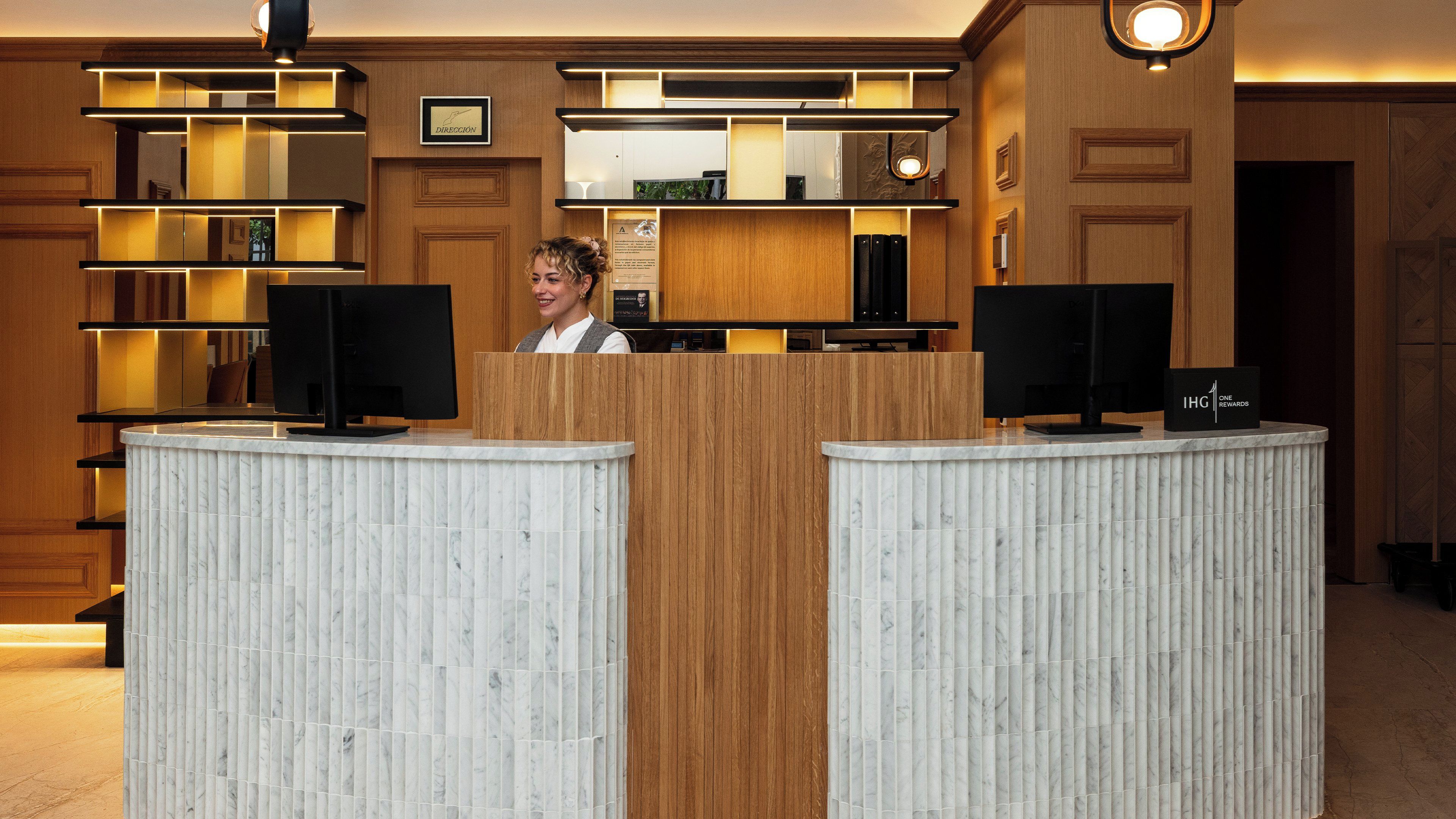 A reception desk with a wooden finish, two black monitors, and a sign reading 'IHG ONE REWARDS'.