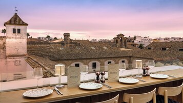 Una mesa de comedor dispuesta con platos, vasos y cubiertos, con vistas a un edificio histórico de tejados de azulejos.