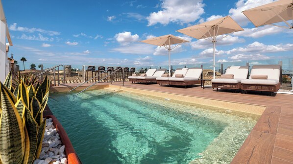A poolside area with lounge chairs and umbrellas, clear water, and a view of the cityscape. - Casa Del Compositor, Vignette Collection by IHG (Jerez de la Frontera)