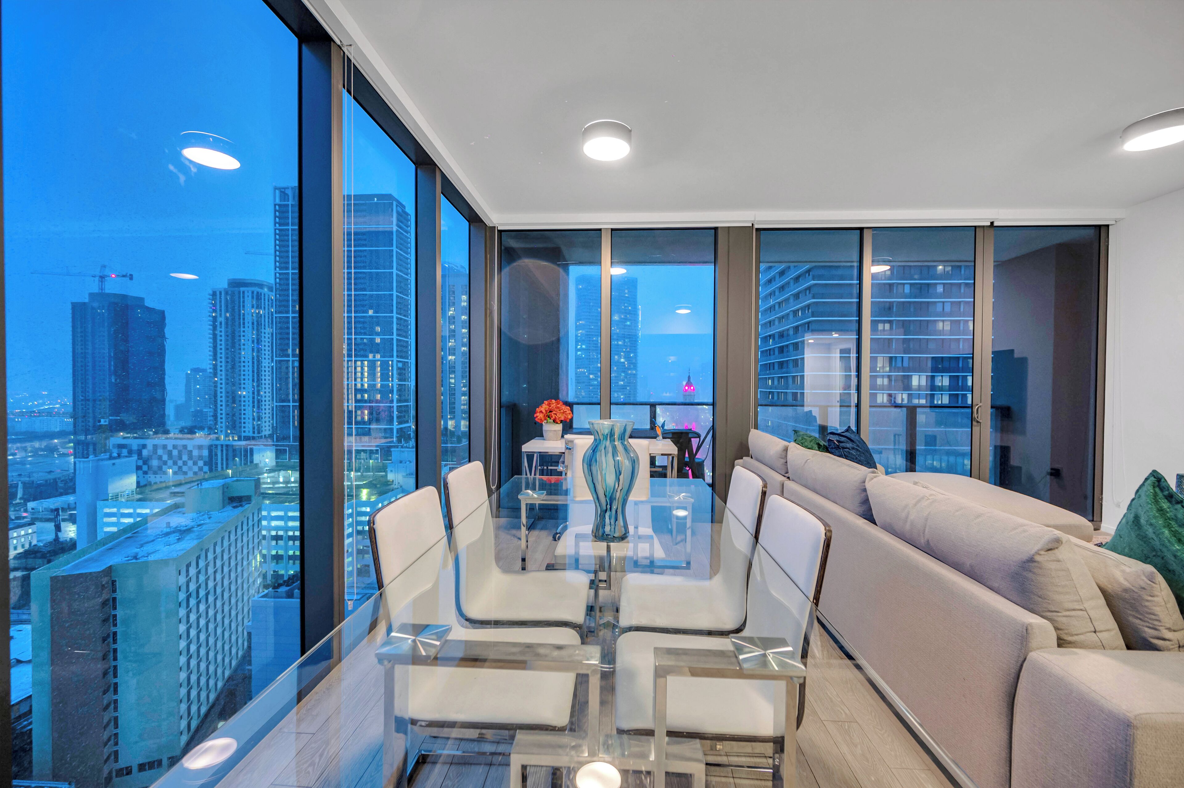 A modern living room with a glass table, white chairs, and a beige sofa.