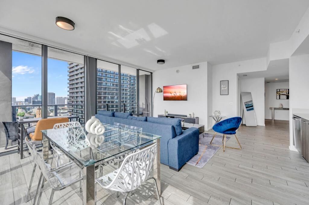 A modern living room with a glass dining table, blue sofa, and a city view.