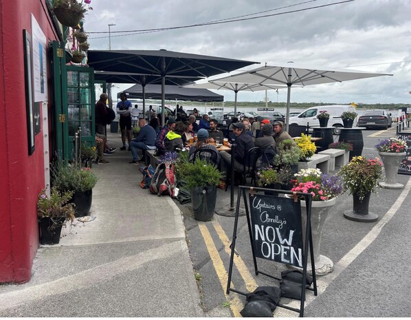 A crowded outdoor seating area with tables and umbrellas, a sign indicating 'Upstairs @ Connolly's NOW OPEN', and potted plants around. - Luxurious seafront 2-bed apt in vibrant Kinvara, Wild Atlantic Way (Kinvarra)