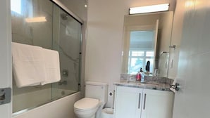 Et moderne badeværelse med et glasafskærmet brusebad, toilet, vask med spejl og et marmorbelagt gulv.