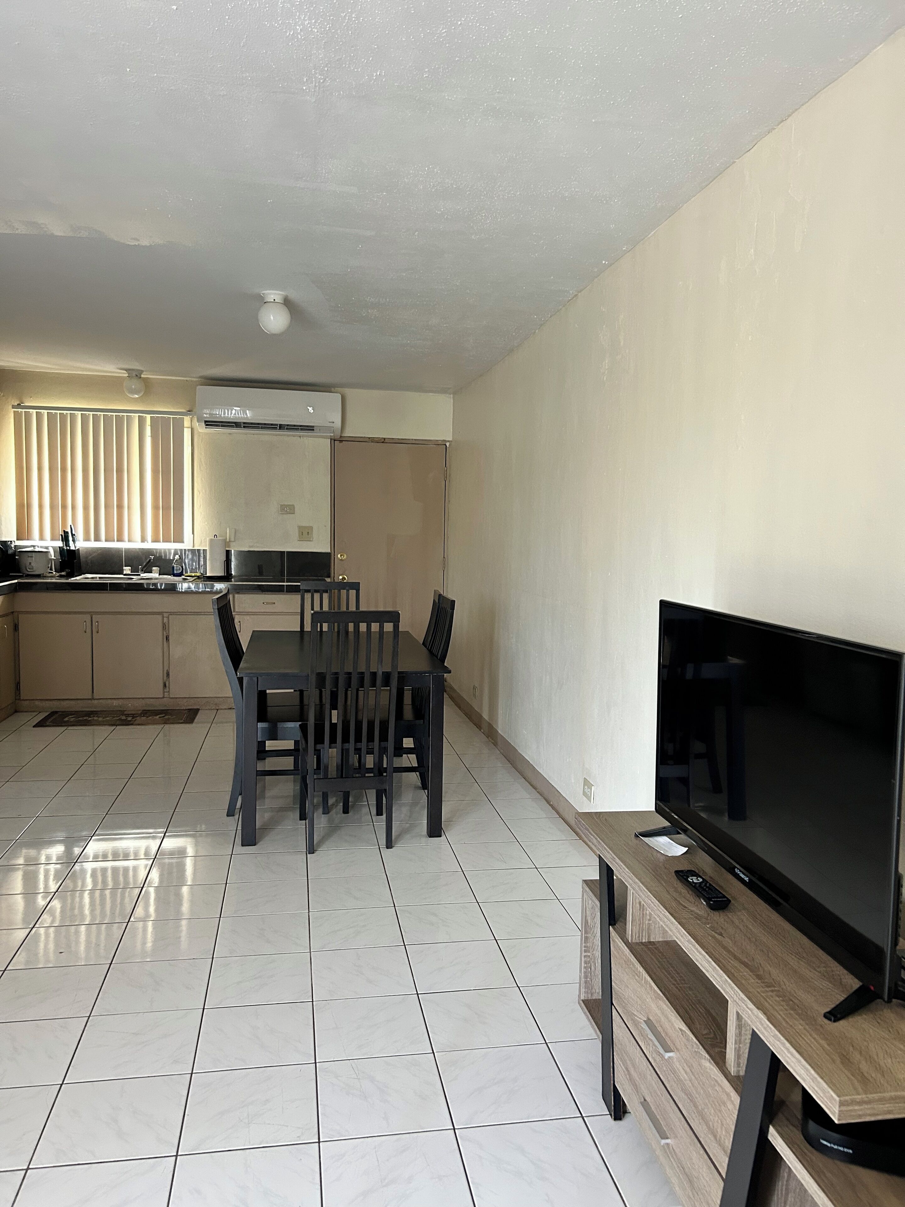 A modern kitchen with a dining area, a flat-screen TV, and a tiled floor.