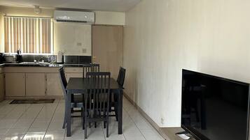 A modern kitchen with a dining area, a flat-screen TV, and a tiled floor.