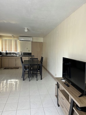 A modern kitchen with a dining area, a flat-screen TV, and a tiled floor.