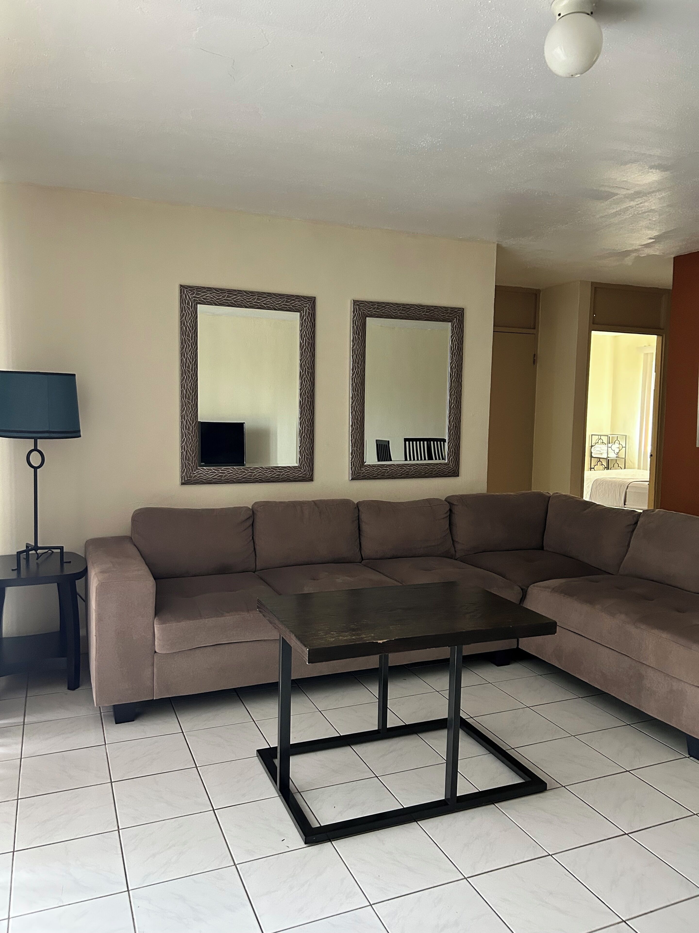 A living room with a brown sofa, a small table, two wall mirrors, a lamp, and a ceiling light.