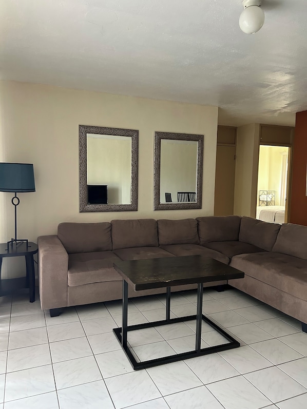 A living room with a brown sofa, a small table, two wall mirrors, a lamp, and a ceiling light.