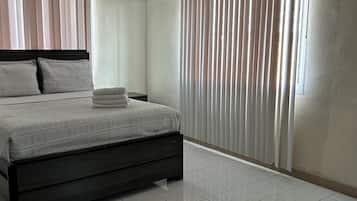 A bedroom with a bed, curtains, an air conditioning unit, and a tiled floor.