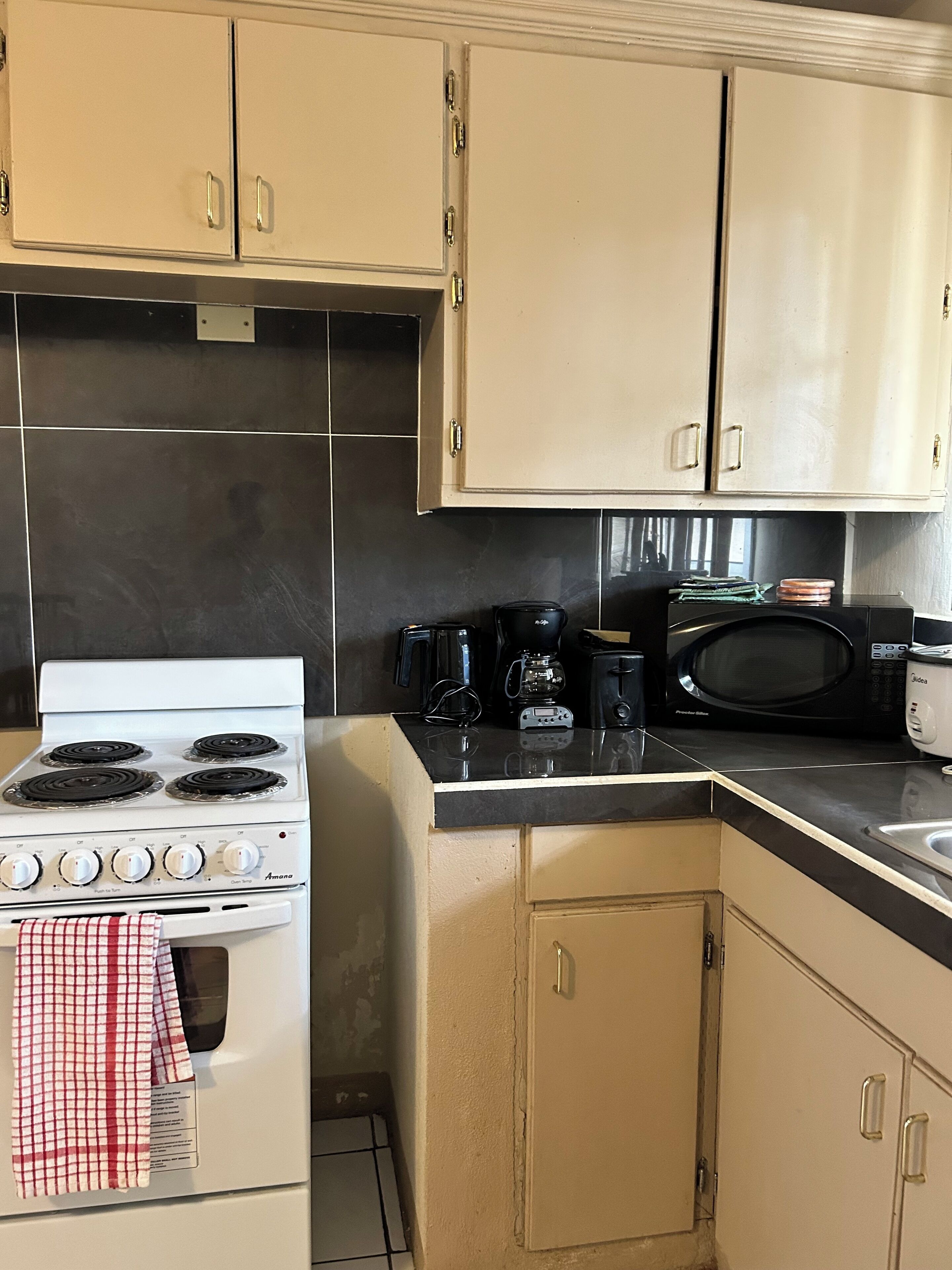 A compact kitchen with a white stove, a microwave, and a coffee maker. There are beige cabinets and a black countertop.