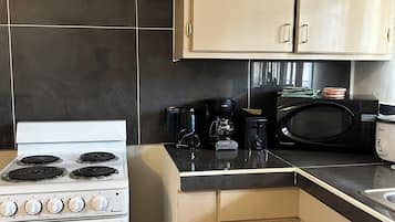 A compact kitchen with a white stove, a microwave, and a coffee maker. There are beige cabinets and a black countertop.