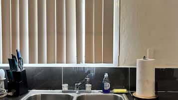 A kitchen with a double sink, a window with vertical blinds, a paper towel holder, and a dish soap bottle.