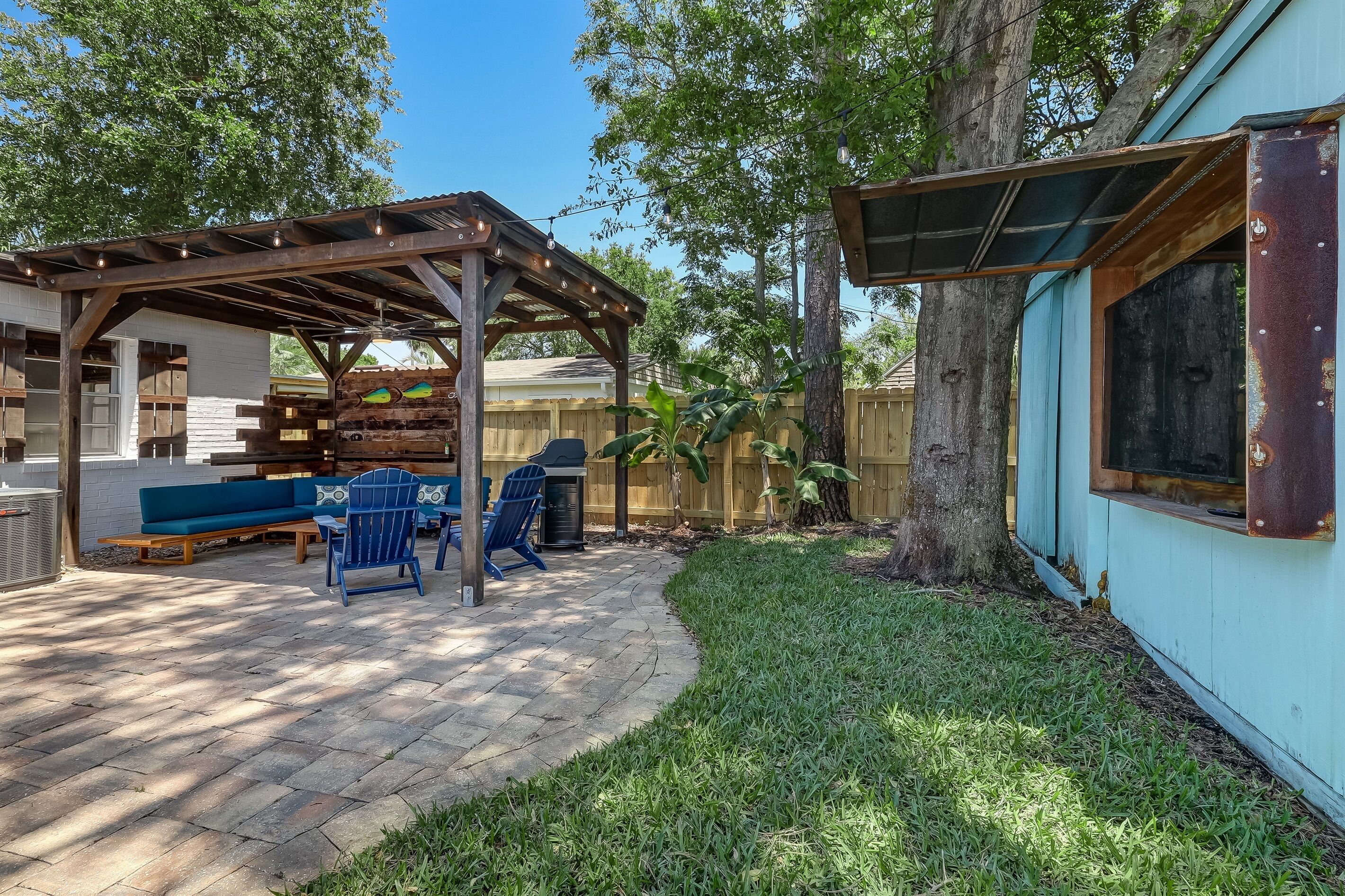 A covered patio area with a wooden bench, chairs, and a grill.