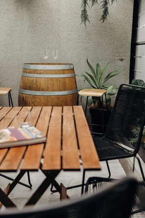A wooden table with chairs, a barrel, and a potted plant in an outdoor setting. - Spacious Newcastle Apartment w parking, pool and gym (Newcastle West)