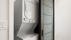 A compact, modern laundry room with a built-in washer and dryer, a wooden door, and a light switch on the wall. - Spacious and private 1-bedroom guesthouse, located near UC Davis Health (Sacramento)