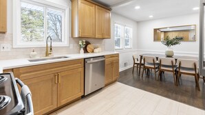 Una cocina moderna con armarios de madera, lavavajillas y comedor con mesa y sillas.