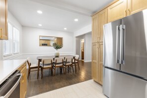 Une cuisine moderne avec des meubles en bois, un réfrigérateur en acier inoxydable et un coin repas comprenant une table et des chaises.