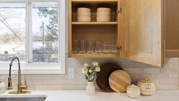 Una cocina con un armario de madera, una ventana, un lavabo y un jarrón con flores.
