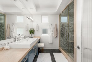 Une salle de bain moderne avec un grand lavabo, deux miroirs, une douche en verre et un petit tabouret.