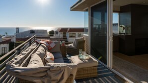 A balcony with a sofa, cushions, and a tray with glasses, overlooking a coastal view. - Ocean View Home | Walk to Beach & Downtown MB (Manhattan Beach)