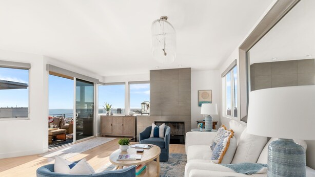 A modern living room with a fireplace, large windows, and a view of the ocean. - Ocean View Home | Walk to Beach & Downtown MB (Manhattan Beach)