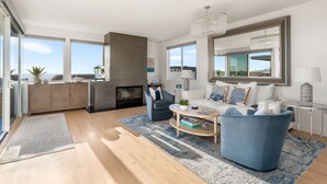 A modern living room with a fireplace, a sofa, a coffee table, and a view of the ocean. - Ocean View Home | Walk to Beach & Downtown MB (Manhattan Beach)