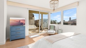 A bedroom with a large bed, a blue dresser, a chair, and a view of the outside. - Ocean View Home | Walk to Beach & Downtown MB (Manhattan Beach)