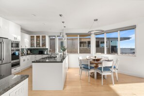 Une cuisine moderne avec des meubles blancs, un îlot central et un coin repas comprenant une table et des chaises.