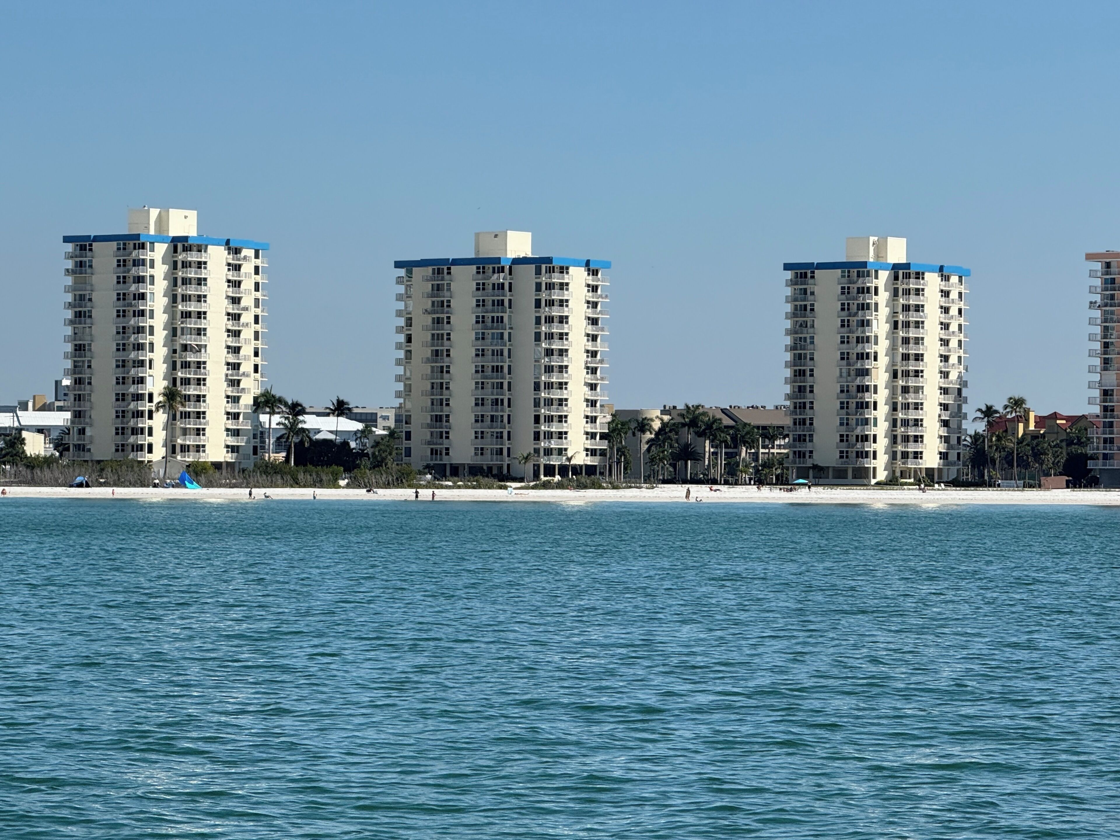A beachfront hotel with multiple high-rise buildings, a sandy beach, and a clear blue sky.