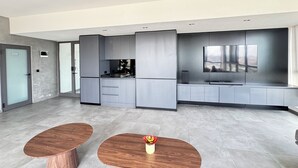 Una cocina moderna con armarios grises, un horno empotrado y un televisor de pantalla plana. Hay dos mesas de madera con un florero.