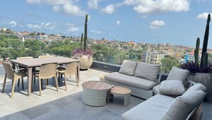 Una terraza en la azotea con una mesa de comedor, sillas, un sofá y una pequeña mesa redonda.
