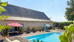 Ein Pool mit Liegestühlen und Sonnenschirmen, ein Gebäude mit Satteldach und Topfpflanzen.