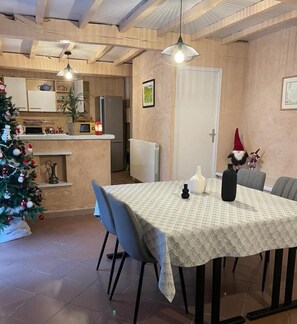 Une salle à manger avec une table dressée pour quatre personnes, un sapin de Noël et une cuisine en arrière-plan.