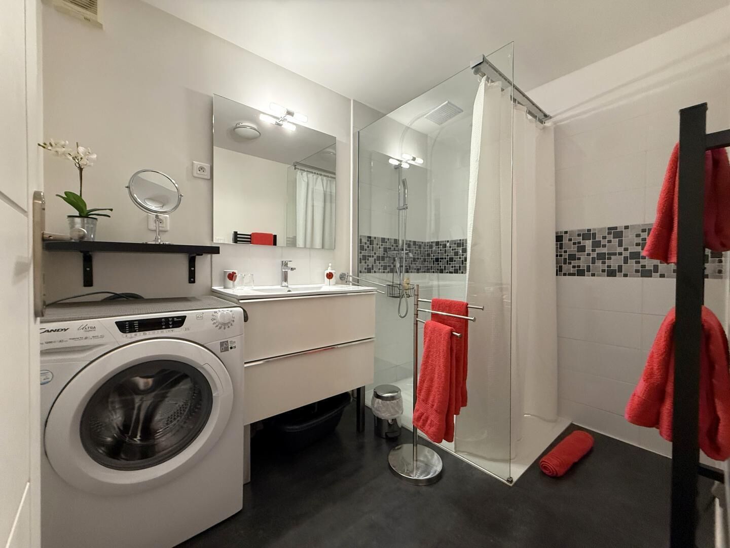 A modern bathroom with a washing machine, a glass shower enclosure, a sink with a mirror, and a towel rack.