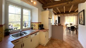 Eine Küche mit Spüle, Herd und Kühlschrank, Holzbalkendecke und einem Essbereich mit Tisch und Stühlen.