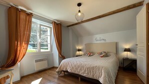 Ein Schlafzimmer mit einem großen Bett, zwei Nachttischlampen, einem Fenster mit Vorhängen, einer Heizung und einem Holzbalken an der Decke.