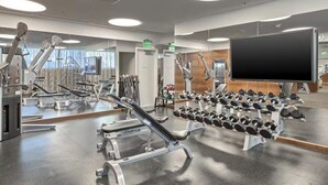Ein Fitnessstudio mit Trainingsgeräten, Spiegeln und einem großen Fernsehbildschirm.