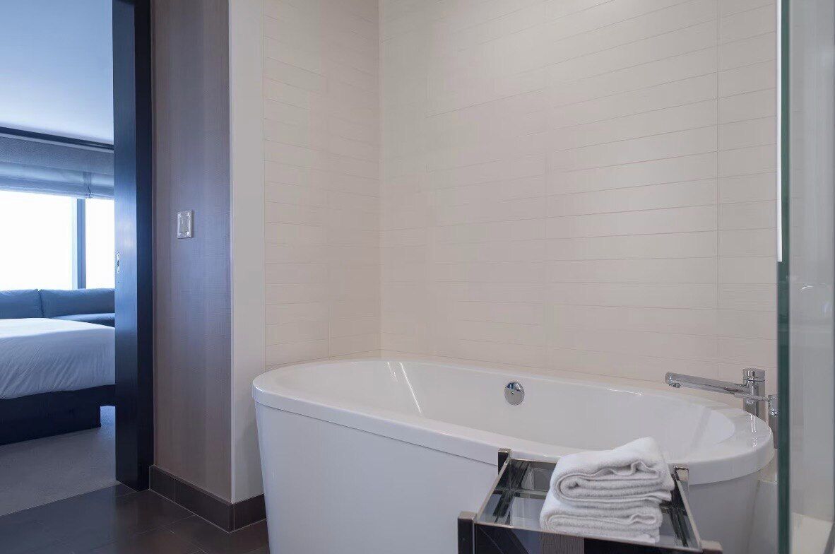 Ein modernes Badezimmer mit freistehender Badewanne, einer Duschkabine aus Glas und einem ordentlich gefalteten Handtuch auf einem Ablagekorb.
