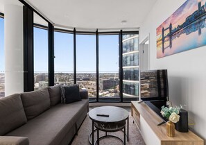 A modern living room with a large window, a sofa, a coffee table, and a flat-screen TV. - City Lights Retreat – Fortitude Valley (Fortitude Valley)
