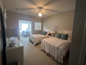 Une chambre avec deux lits, un ventilateur de plafond, un bureau avec une lampe et une vue sur un balcon.