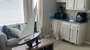 Ein Wohnzimmer mit einem Modell eines Segelboots, einer Couch, einer Kaffeemaschine und einer Küchenzeile mit Schränken.