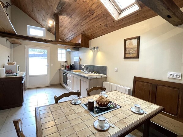 A kitchen with a dining area, wooden ceiling, and a view through the window. - GITE DE L'ISARCE - MONTAUT (MONTAUT)